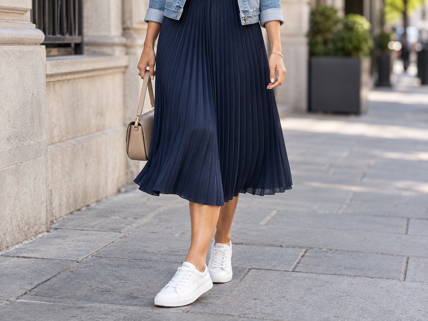 Detaliu: femeie în rochie midi plisată bleumarin cu jachetă din denim și teniși, în oraș